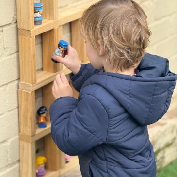 Child in blue jacket playing with toys on a wooden shelf.