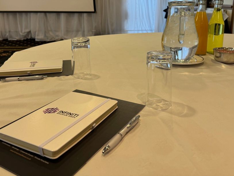 Conference room setup with notebooks, pens, and beverages on a round table.