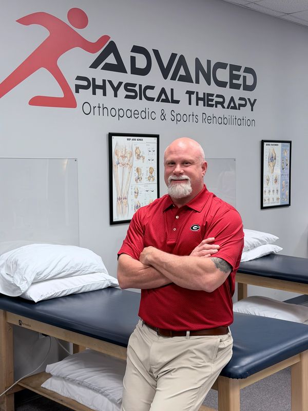 Man in red shirt stands confidently in a physical therapy clinic.