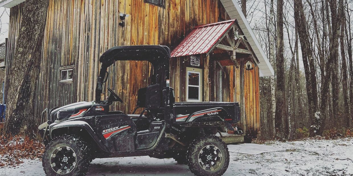 A black Kubota off-road utility vehicle parked by a wooden cabin in a snowy forest.
