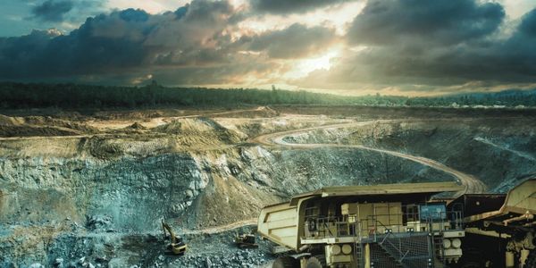 Large mining dump truck and excavators at an open-pit mine during sunset.