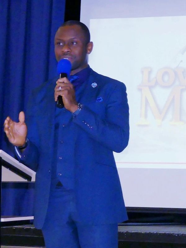Man in a blue suit speaking into a microphone on stage.