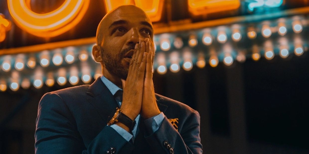 A photo of hypnotist Chris Jones with his hands in a prayer position, outside a theater at night.