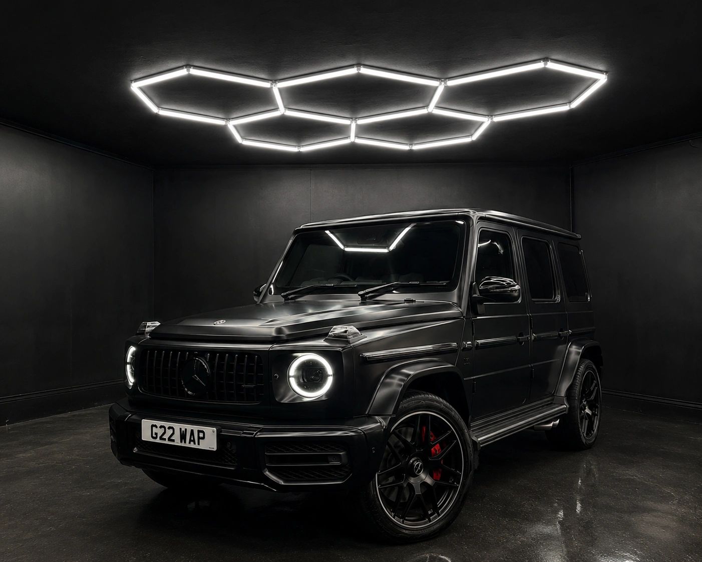 Sleek black Mercedes G-Wagon under hexagonal ceiling lights in a dark room.