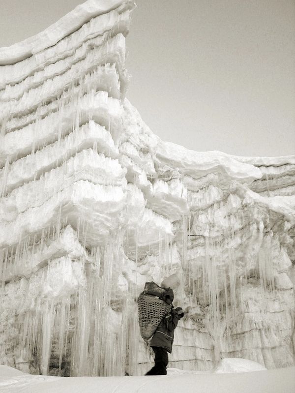 Person standing near massive icy cliffs with hanging icicles.