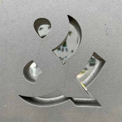 Metal surface with an ampersand cutout showing blurred background.