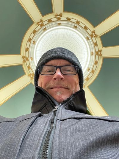 Man wearing glasses and a beanie under a decorative dome ceiling.