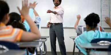 Teacher engaging with students who are raising their hands in a classroom.