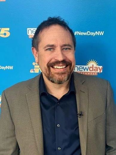 Man smiling in front of a New Day Northwest backdrop.