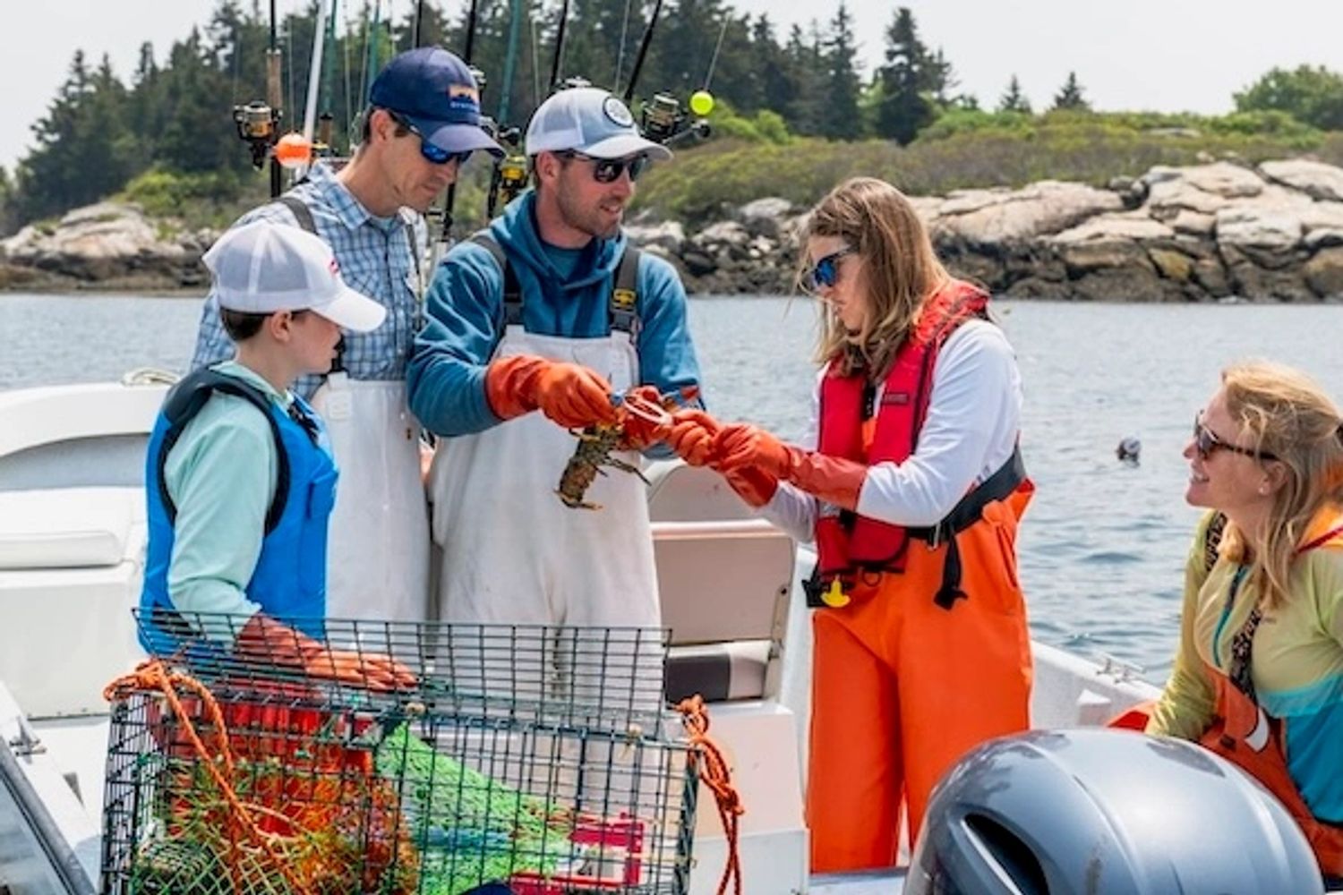 A family of 4 looking at a lobsterman holding a lobster on a Casco Bay charter