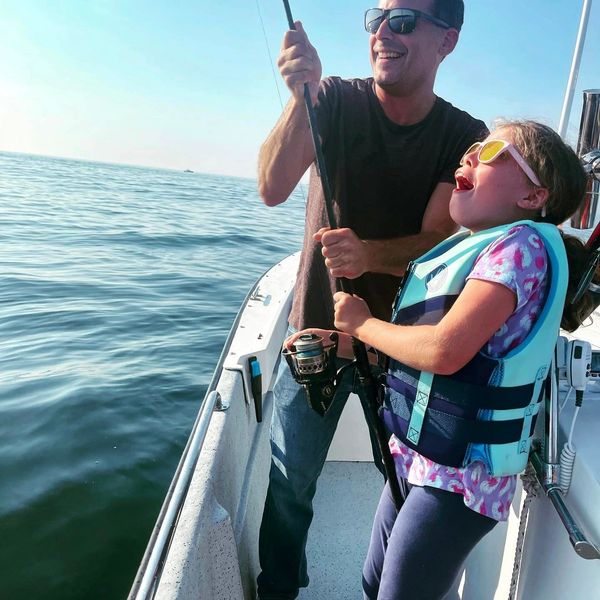 A father and daughter holding one fishing rod as they reel in a fishing together in Casco Bay, Maine