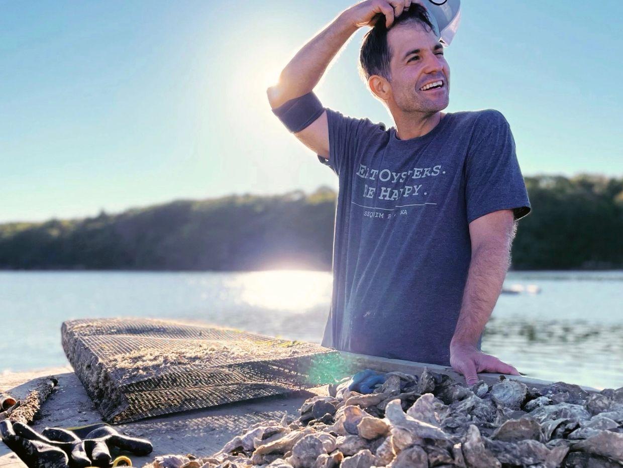John Herrigel standing at his oyster farm table sorting through a pile of oysters