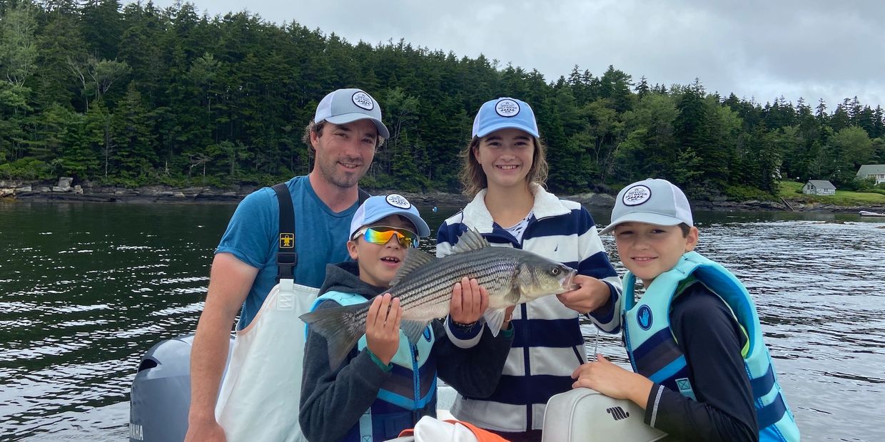 Captain Joe with 3 kids holding up a striper on a family fishing charter in Maine