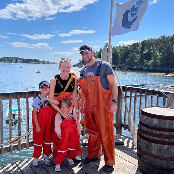 A family of 4 standing on a dock in Phippsburg Maine wearing lobsterman fishing bibs.