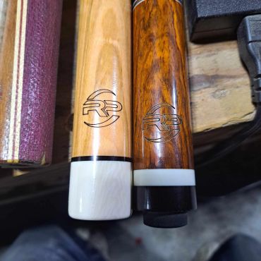 Two wooden cue sticks with matching logos and contrasting white and black tips.