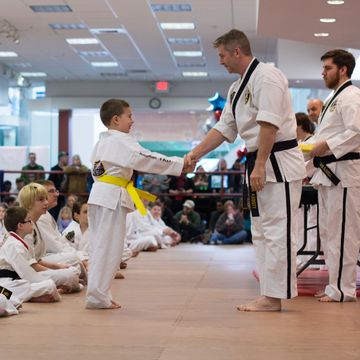 A young boy receives a karate belt from an instructor during a ceremony.