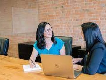 Two women collaborating in a modern office setting with a laptop and notebook.