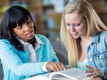 Two young women studying together and looking at a book.