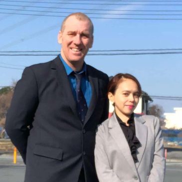 A man and a woman in formal attire posing outdoors on a sunny day.
