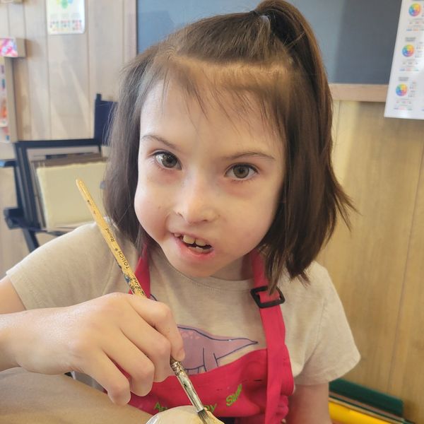 A young girl painting a clay ball in an art class.