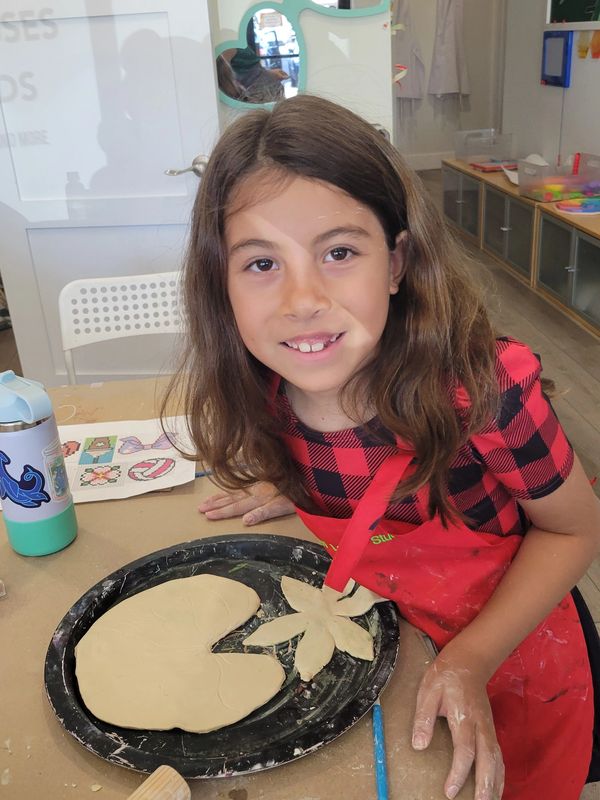 Young girl smiling with clay art in a classroom setting.