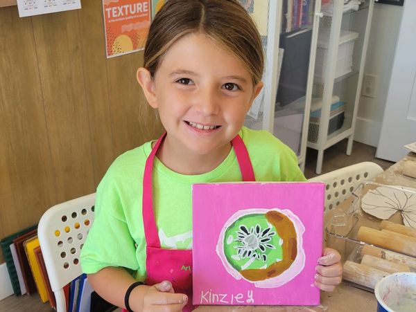 Young girl proudly displays her colorful painting in an art classroom.
