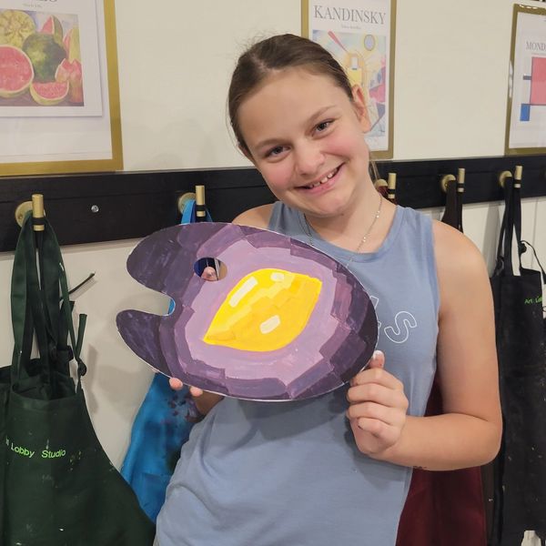 Smiling girl showing a colorful painted palette in an art studio.