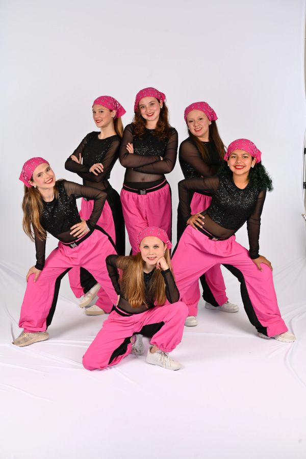 A group of six girls in matching pink and black dance outfits posing confidently.