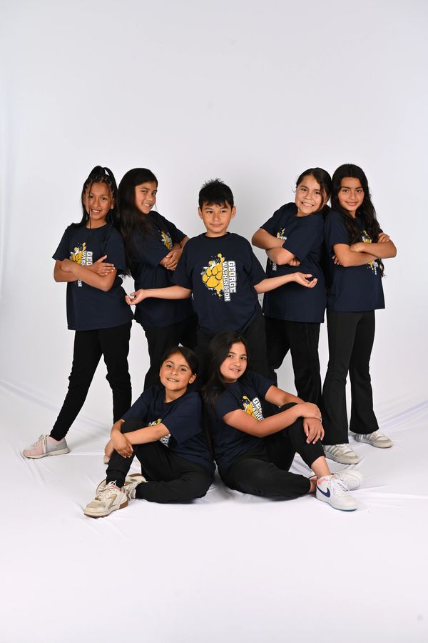 Seven children in matching navy blue shirts posing confidently against a white background.