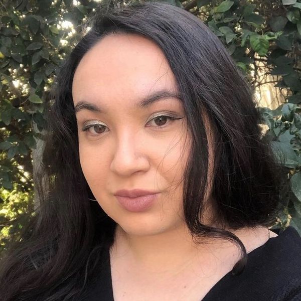 Close-up portrait of a woman with long dark hair and natural makeup outdoors.