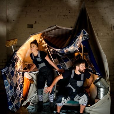 Two people in creative costumes inside a makeshift tent with lights.