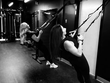 Two women exercising with suspension straps in a gym.
