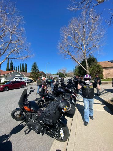Group of motorcyclists and their bikes parked on a suburban street on a clear day.