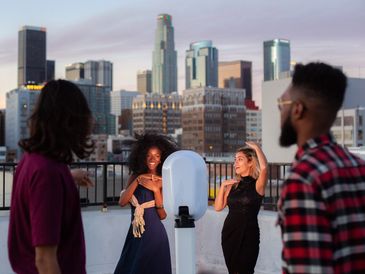 Group of people standing on a rooftop in the city taking photos in front of a photo booth.