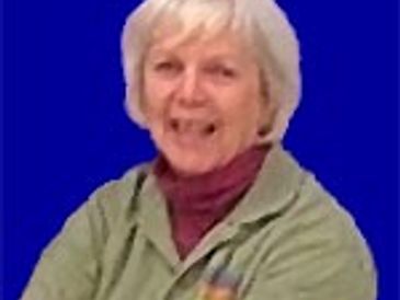 An elderly woman smiling against a blue background.