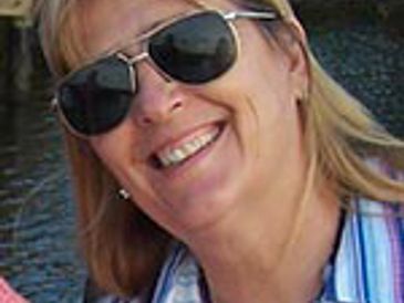 Smiling woman wearing sunglasses outdoors near water.