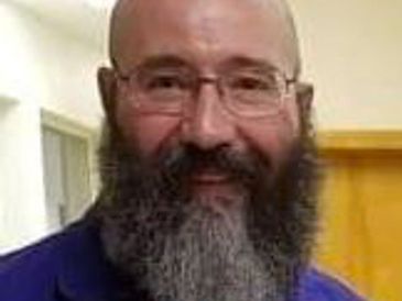 Man with glasses and a thick beard smiling indoors.