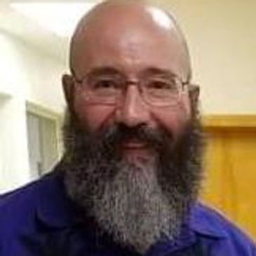Man with glasses and a thick beard smiling indoors.