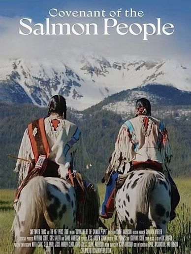 Two Native American riders on spotted horses with snowy mountains in the background.