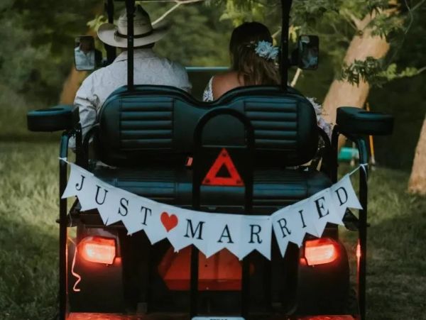 Newlyweds riding a golf cart with a 'Just Married' sign on the back.