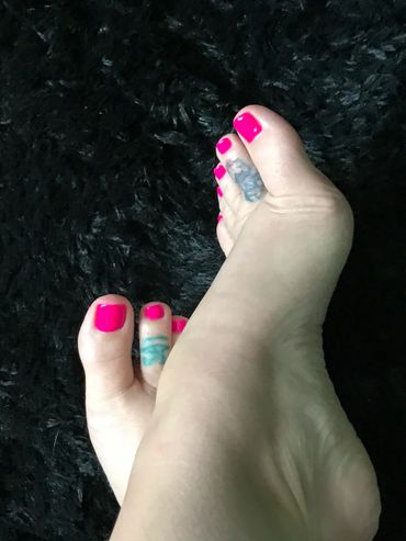 Feet with bright pink nail polish and toe tattoos on a black textured background.