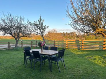 Outdoor dining table with chairs on a grassy lawn at sunset.