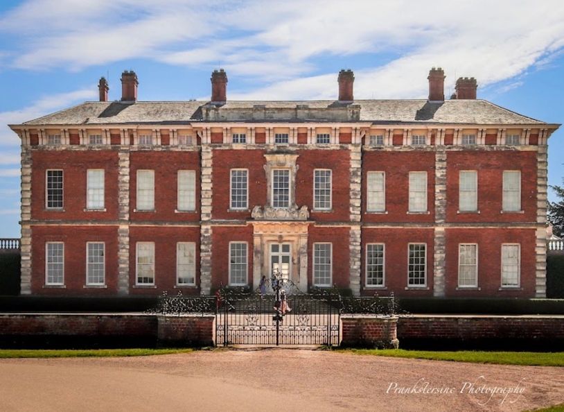Historic large red brick mansion with ornate stone accents and gated entrance.