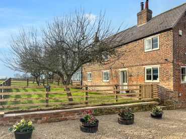 Brick farmhouse beside a fenced yard with leafless trees under a clear sky.