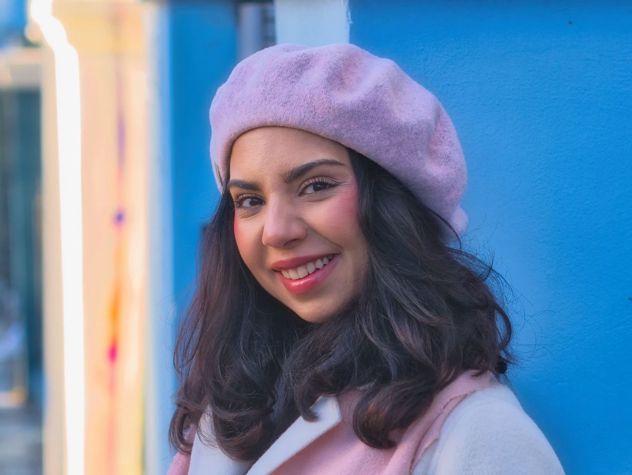 Young woman smiling in a pink beret against a blue wall.