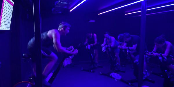 Group cycling class with blue neon lighting and focused participants.