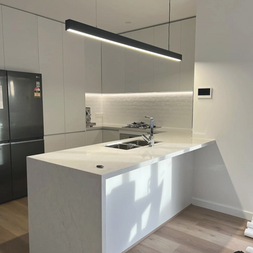 Pendant strip light above island bench in white kitchen and under-cabinetry strip lighting 
