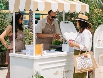 A woman buys food from two vendors at an outdoor stall.