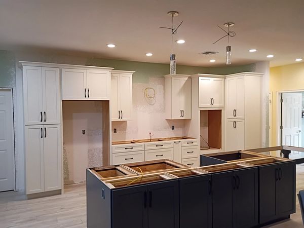Kitchen under construction with white and dark cabinetry and exposed wiring.