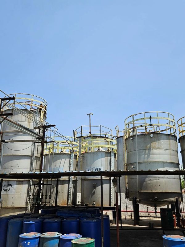 Large industrial storage tanks and blue barrels under clear sky.
